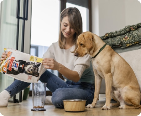 En kvinna häller Hill's Pet Nutrition-mat i ett mått medan en hund tittar uppmärksamt.