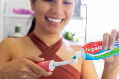 En kvinna som ler samtidigt som hon sätter Colgate-tandkräm på en tandborste i ett badrum.